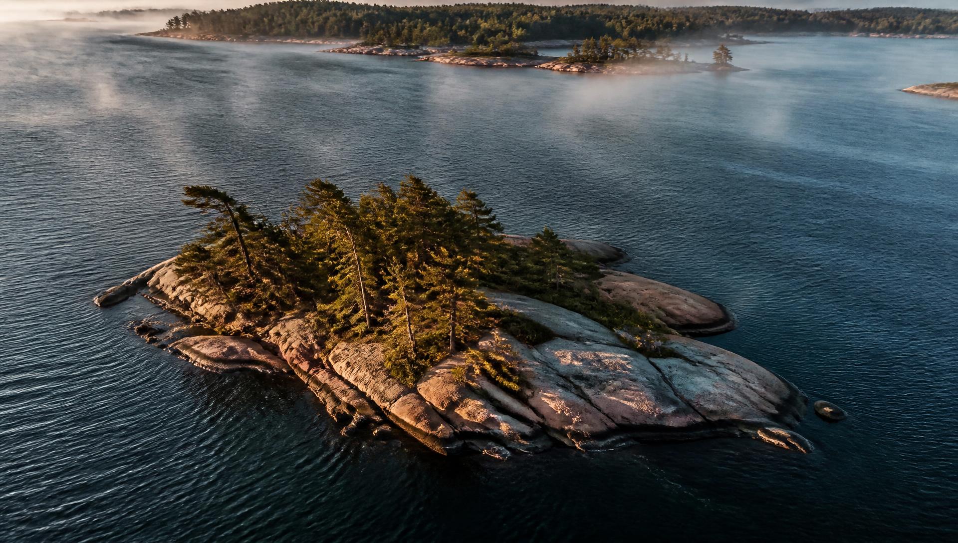 Aerial view of a pine-covered granite island in Georgian Bay at golden hour